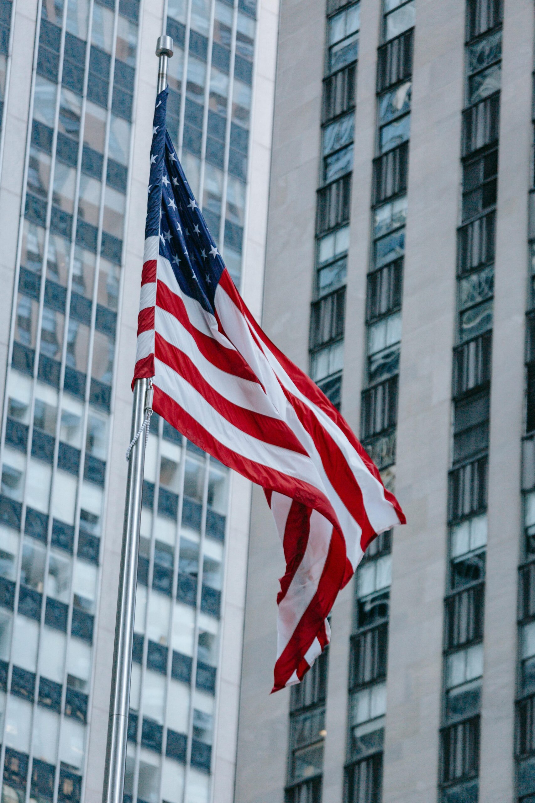 From below national US flag waving on pole against modern skyscraper in urban city district